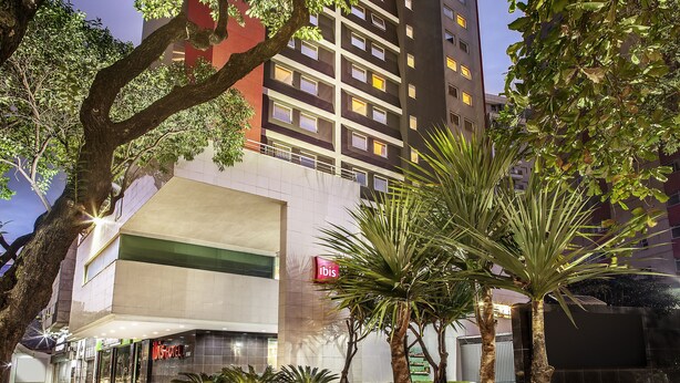 A hotel with a modern facade, a prominent 'ibis' sign, and a well-maintained outdoor area with palm trees and a landscaped garden. - Ibis Belo Horizonte Savassi (Belo Horizonte)