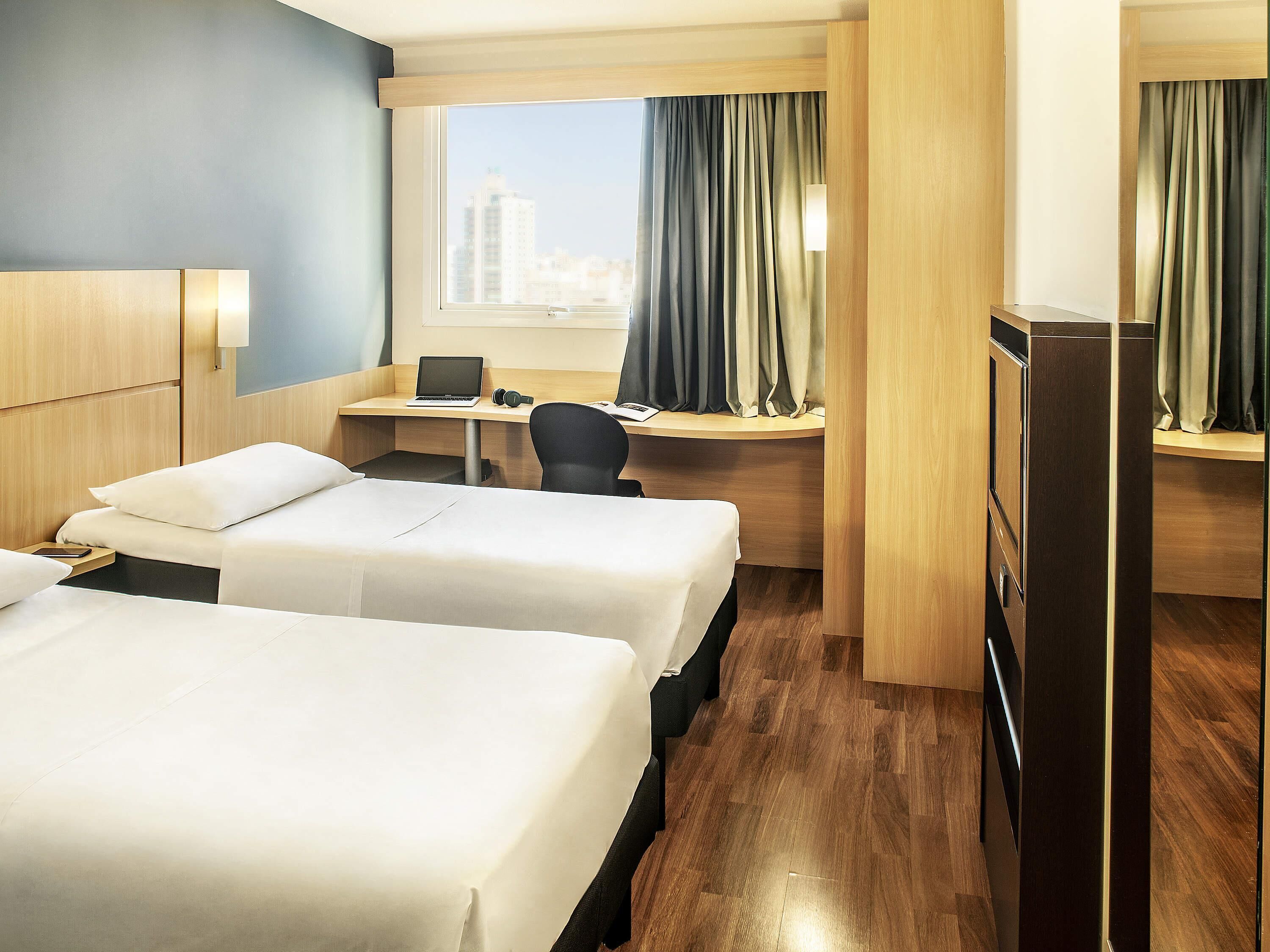 A hotel room with two beds, a desk with a laptop, a chair, and a TV.