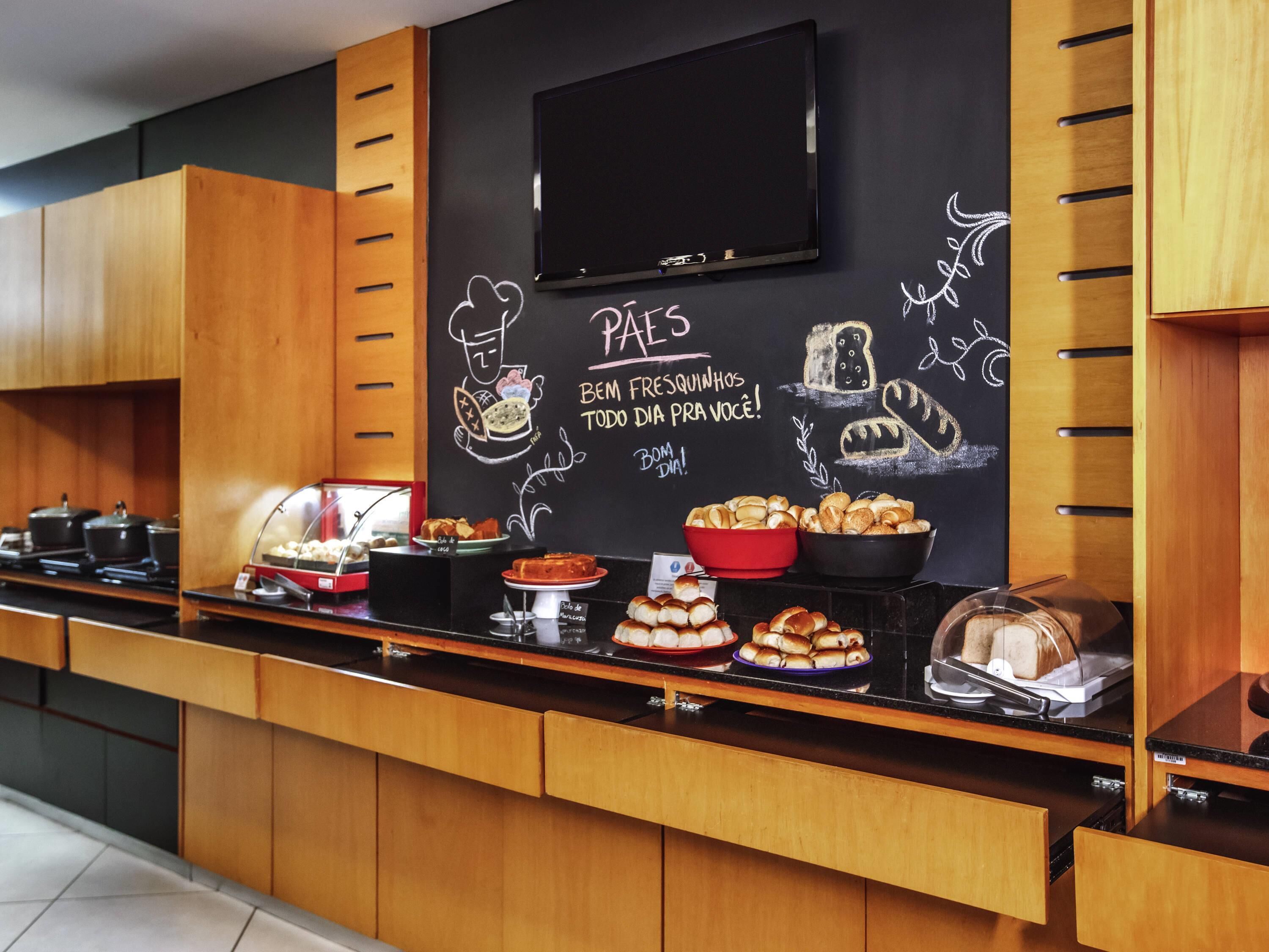 A buffet counter with various food items, a chalkboard with drawings and text, and a television above.