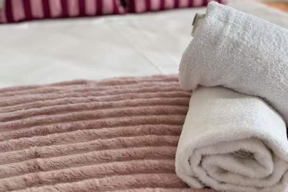A neatly made bed with a folded white towel on a pink textured blanket.
