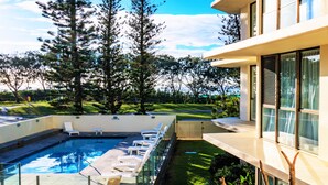 A modern outdoor swimming pool with lounge chairs, surrounded by greenery and tall trees. - Seacrest Beachfront Holiday Apartments (Surfers Paradise)