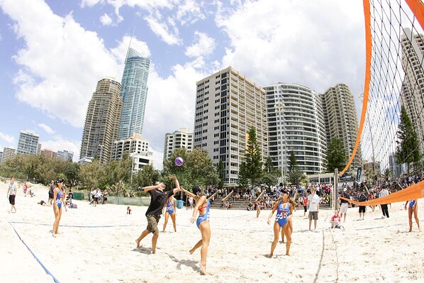Un partido de voleibol de playa con jugadores en trajes de baño y espectadores al fondo.