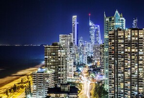 Un paisaje urbano nocturno con rascacielos, una playa y una carretera con estelas de luz.