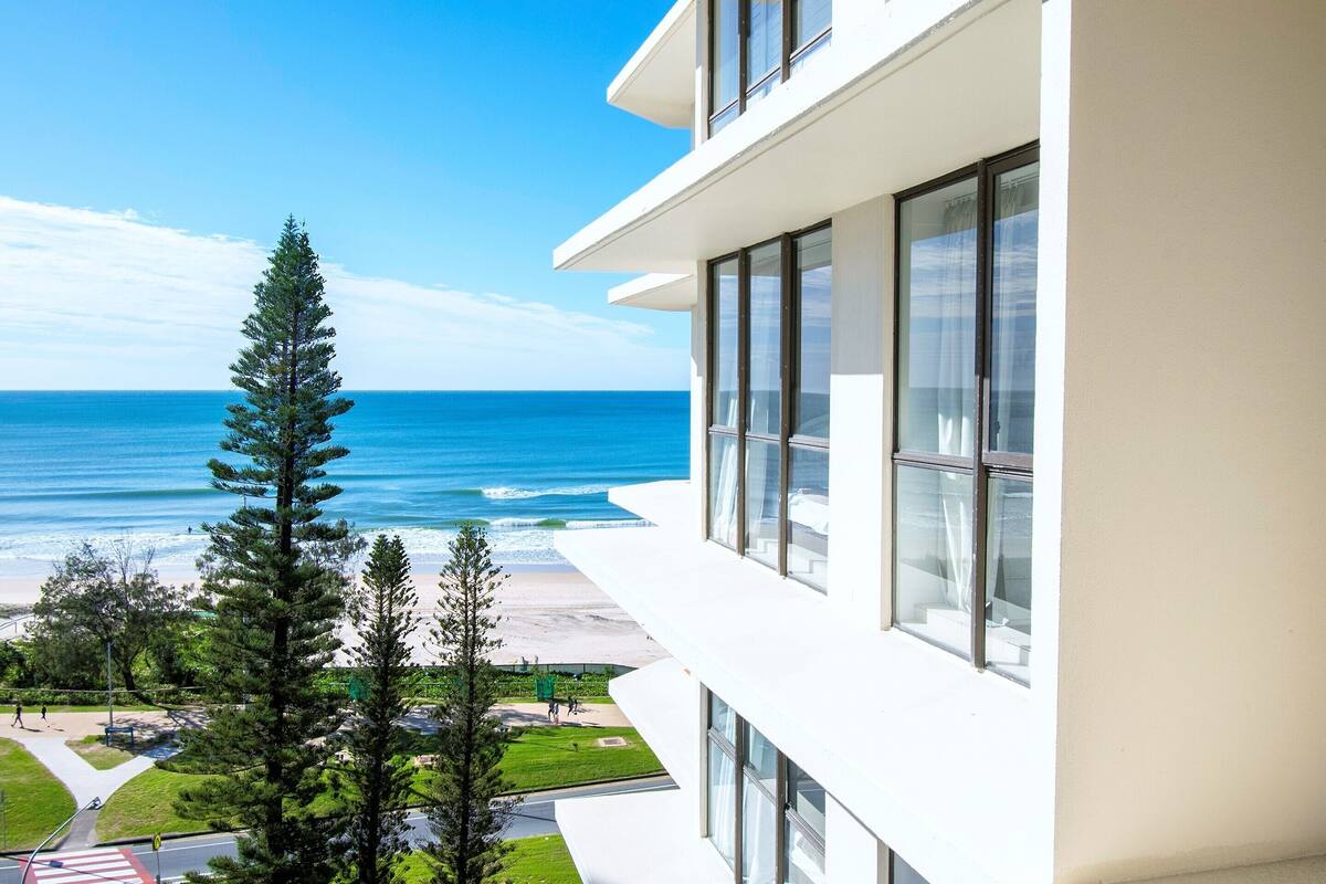 A modern building with large windows overlooking a beach and ocean.