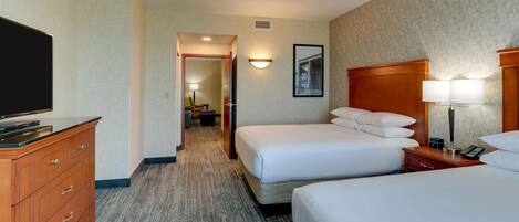 A hotel room with two beds, a TV, a dresser, and a hallway leading to a bathroom.