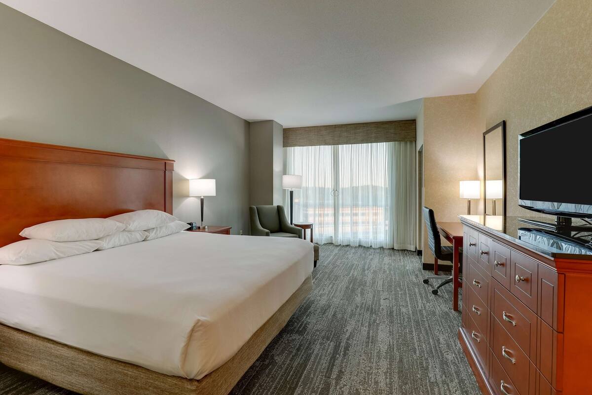 Una habitación de hotel con una cama grande, un escritorio, una silla, un televisor y un aparador.