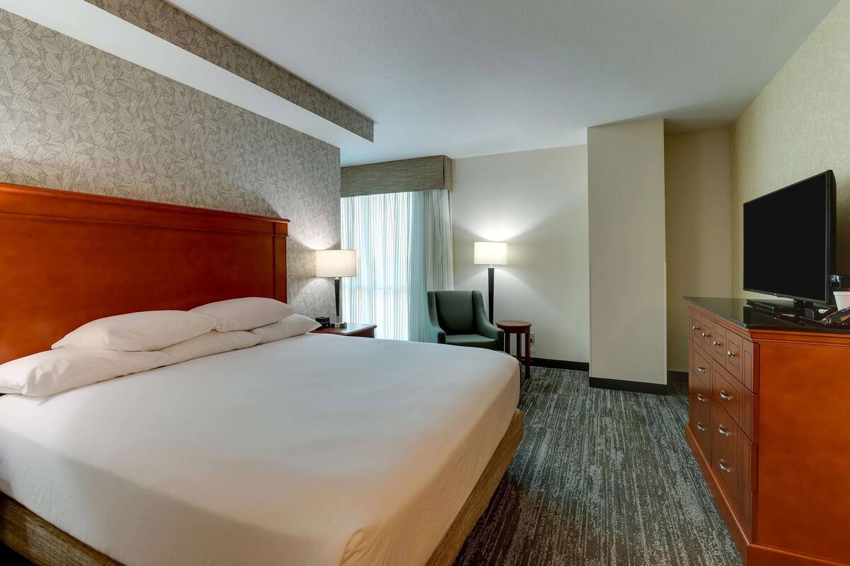 Una habitación de hotel con una cama grande, cabecera de madera, escritorio con televisor y una silla.