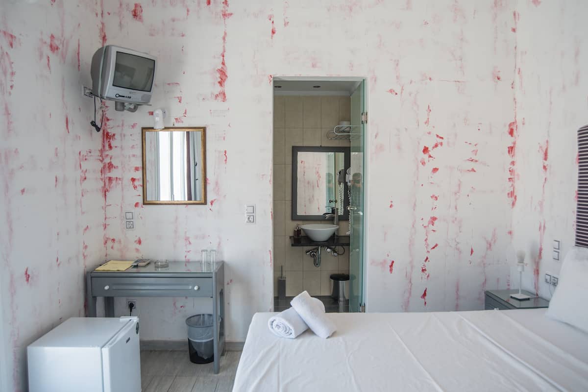 Habitación de hotel con cama, un escritorio pequeño, televisión, espejo y baño visible a través de una puerta abierta.