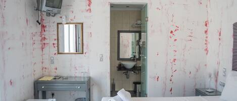 Habitación de hotel con cama, un escritorio pequeño, televisión, espejo y baño visible a través de una puerta abierta.
