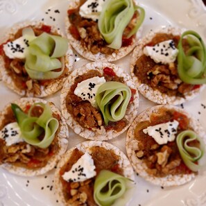 A plate of food with rice crackers topped with a mixture of ingredients and garnished with green leaves and black seeds.