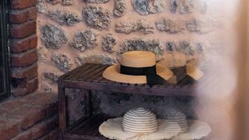 A rustic interior with a stone wall, a wooden table with hats, and a brick fireplace.