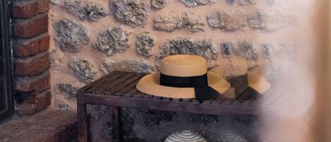 A rustic interior with a stone wall, a wooden table with hats, and a brick fireplace.