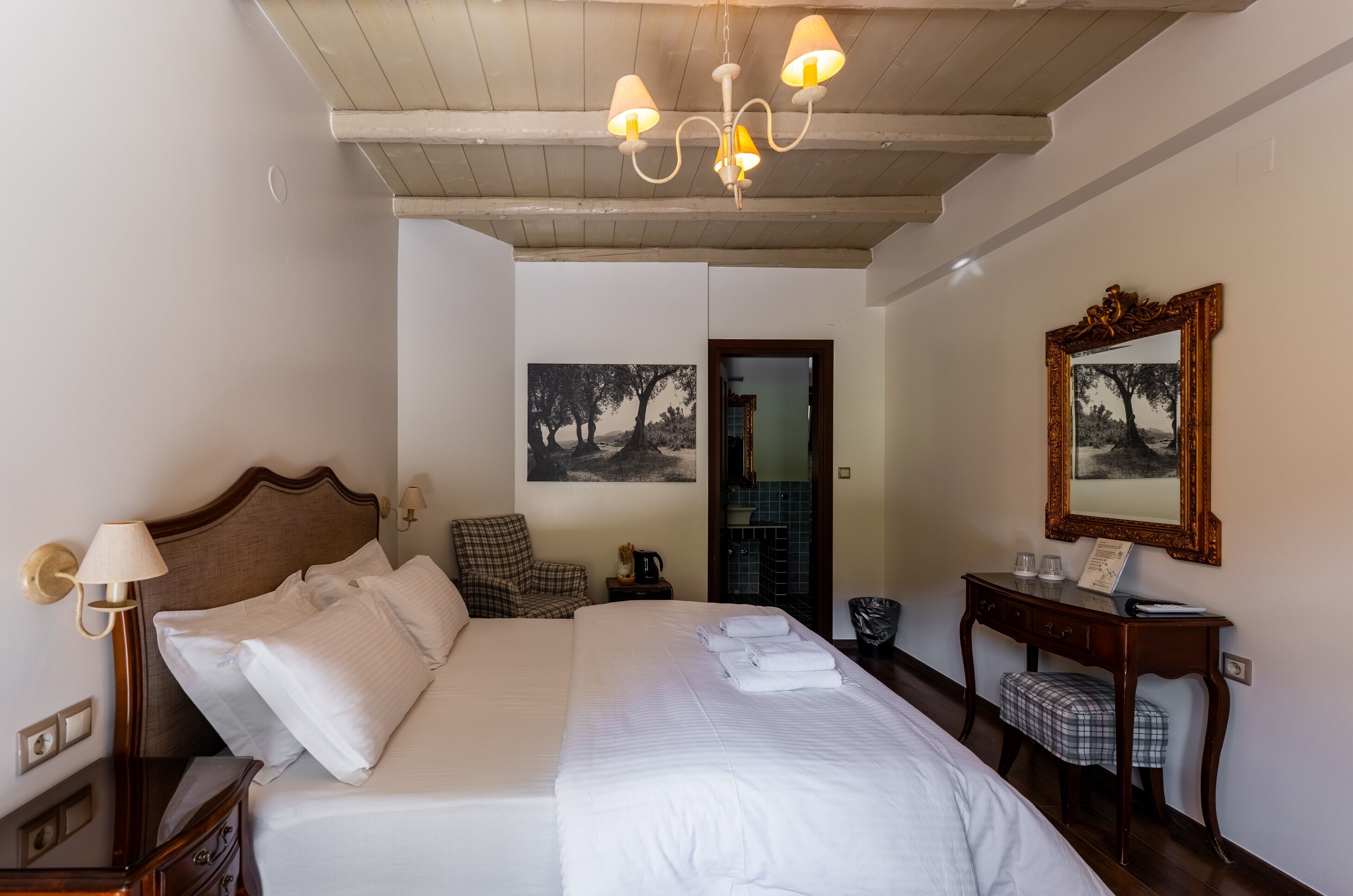 A hotel room with a large bed, a desk with a mirror, and two wall-mounted lamps.