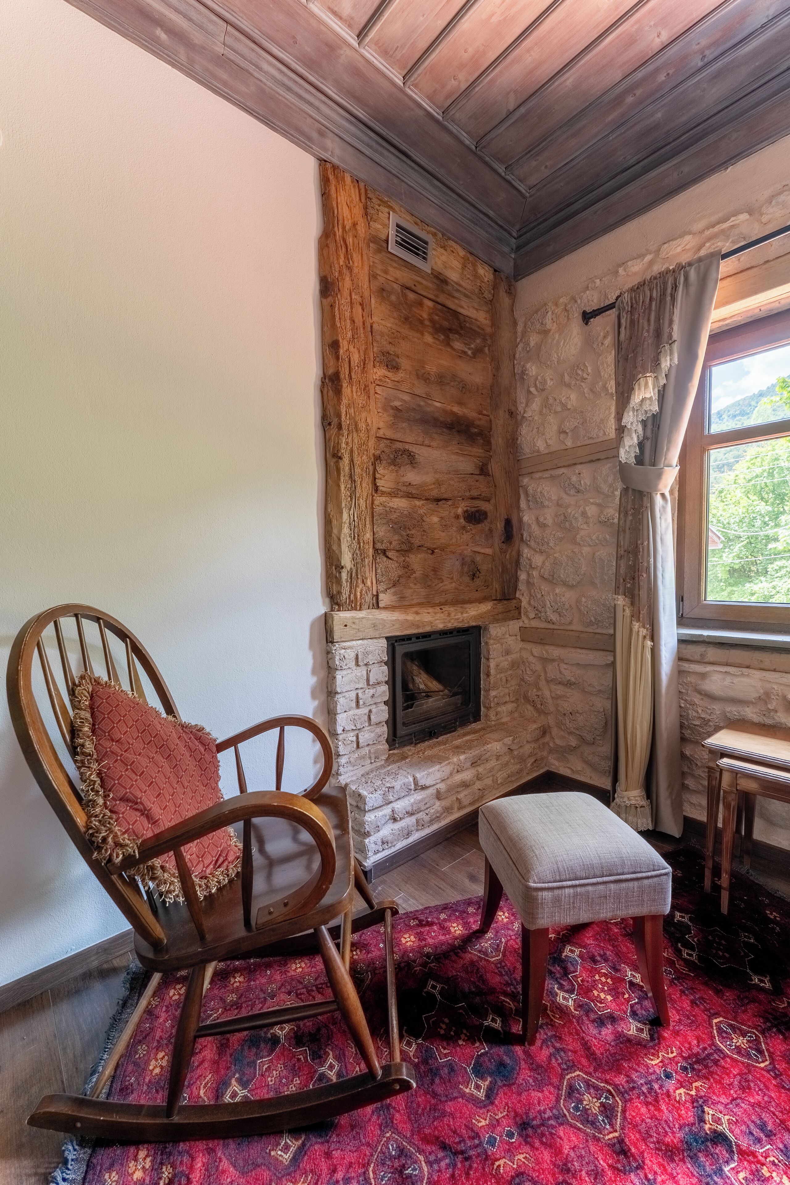 A cozy room with a wooden rocking chair, a small ottoman, and a stone fireplace.