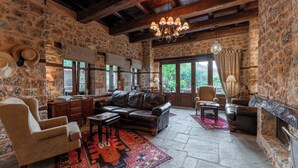 A rustic stone-walled room with a leather sofa, armchairs, a fireplace, and a chandelier. - To Palio Litohoro (Dio-Olympos)