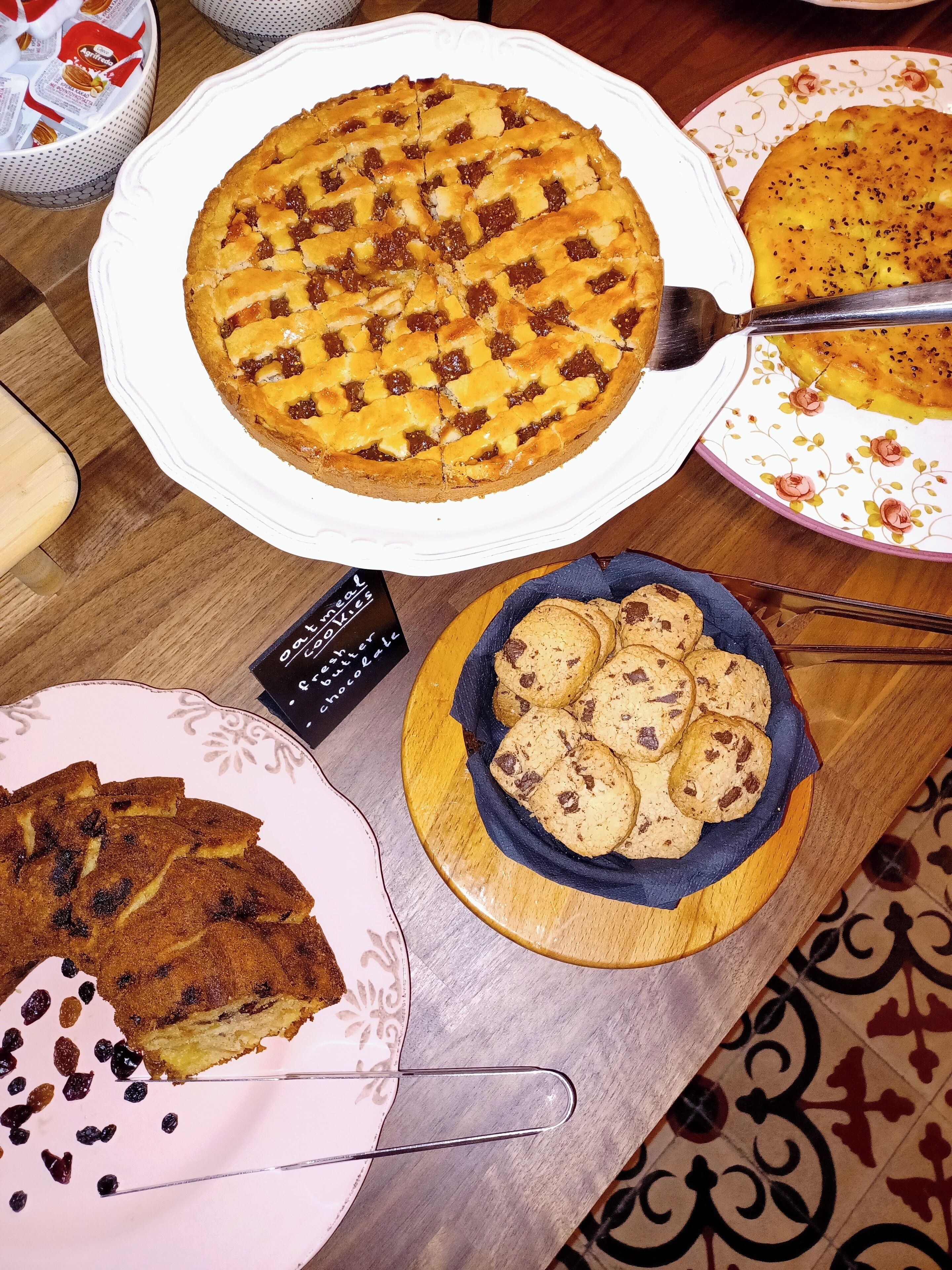 A table with various desserts including a lattice-topped pie, a slice of cake, and a bowl of cookies.