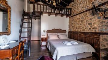 Un dormitorio con una cama de madera, un escritorio con silla, una escalera, una araña y una pared de piedra.