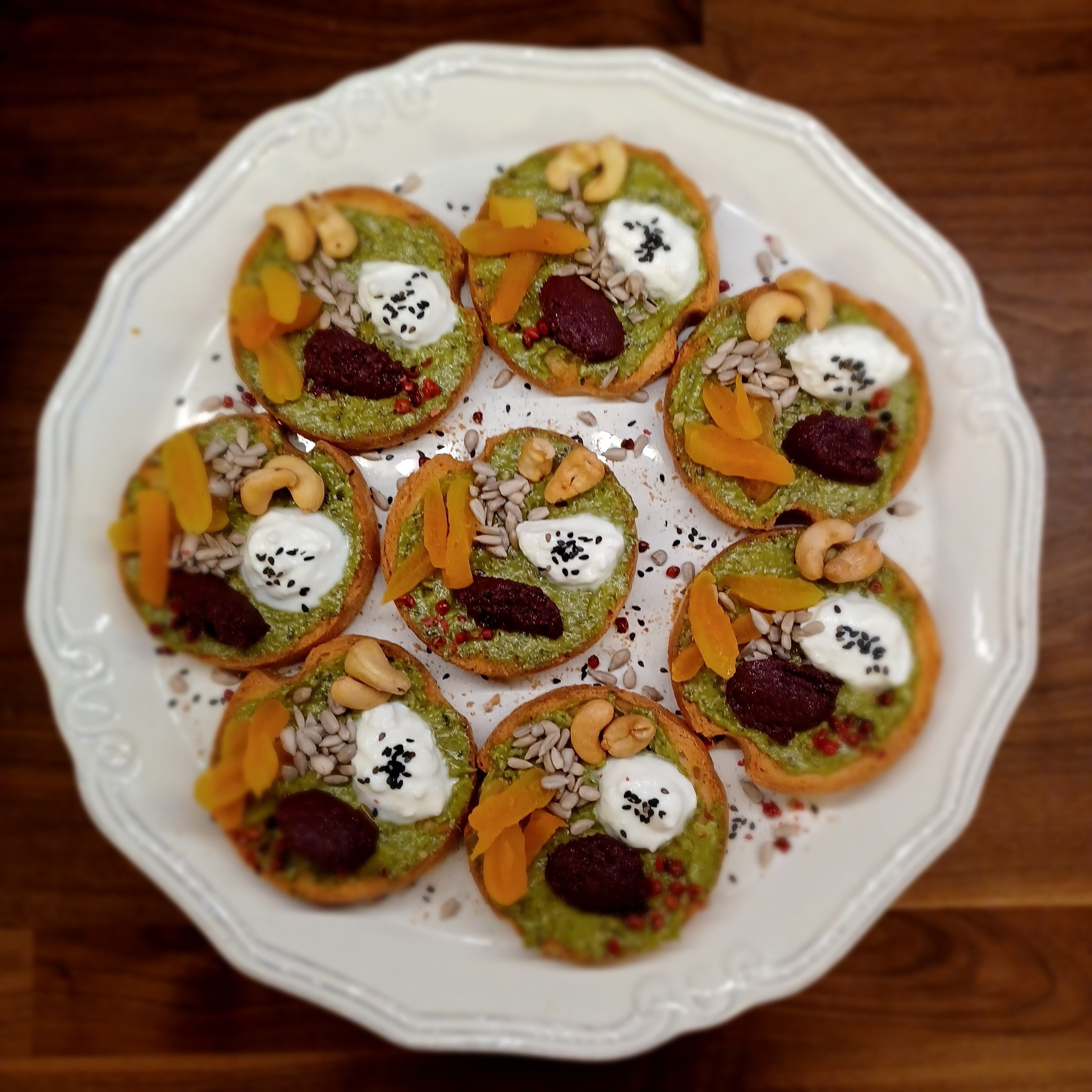 Un piatto bianco con diversi pasticcini ricoperti da una crema verde, noci e frutta secca.