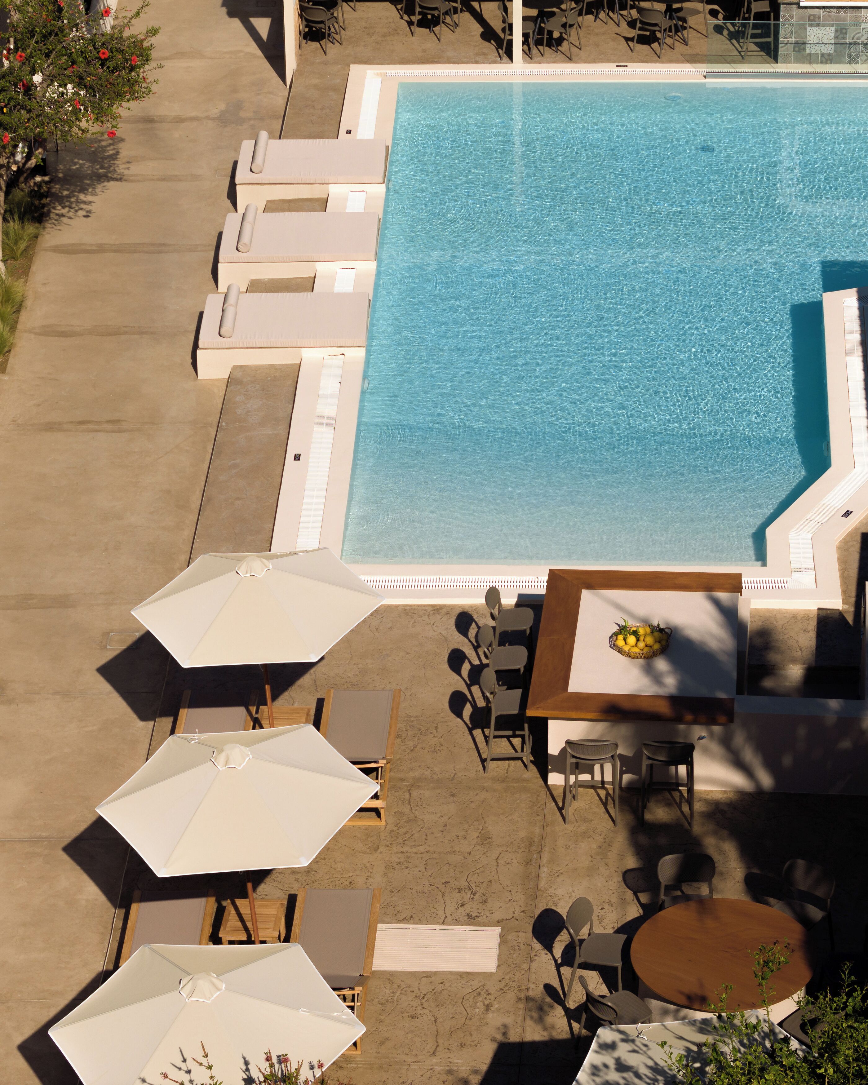 An aerial view of a pool area with lounge chairs, umbrellas, and a table with chairs.