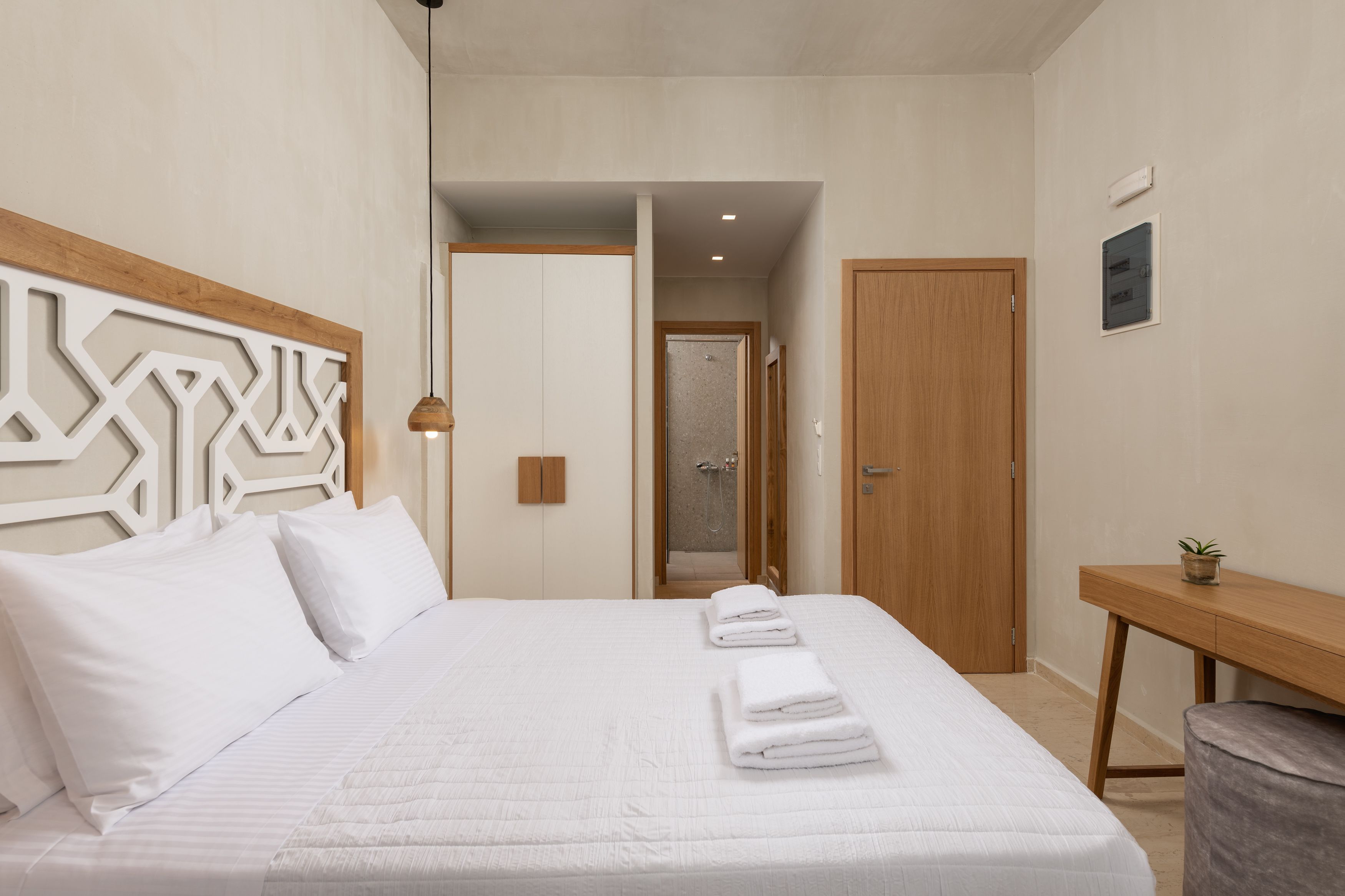Una habitación de hotel moderna con una cama grande, un cabecero de madera, un escritorio pequeño y una zona de ducha.