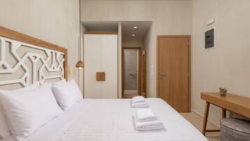 Una habitación de hotel moderna con una cama grande, un cabecero de madera, un escritorio pequeño y una zona de ducha.