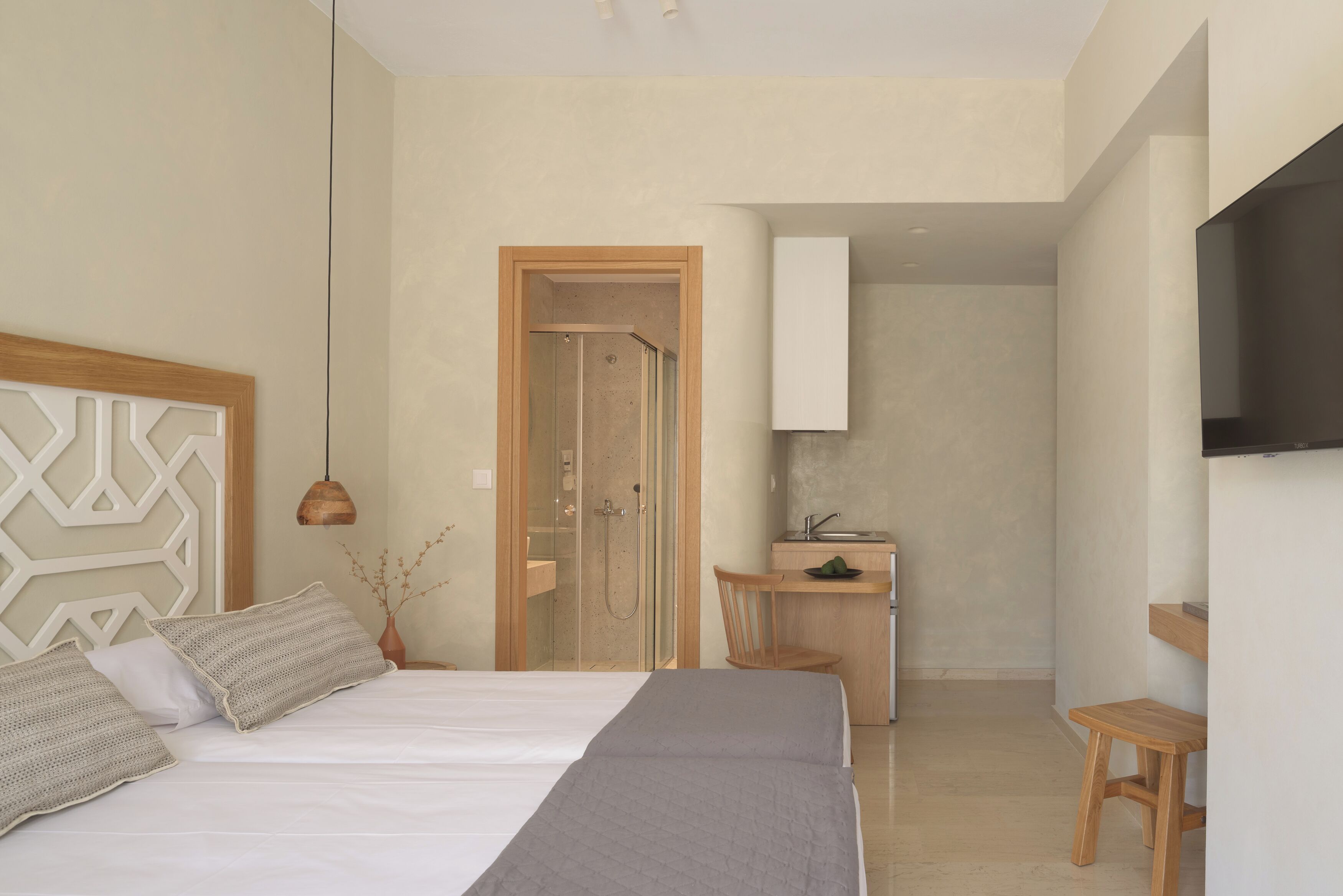 Un dormitorio moderno con una cama grande, un cabecero de madera, un escritorio pequeño y una zona de ducha.