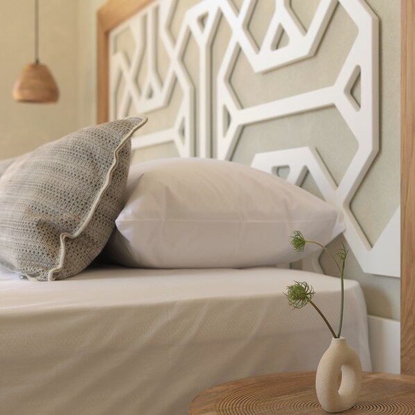 A bed with a geometric wall design, a textured pillow, and a vase with a plant. - Apollo Apartments (Agios Vasileios)
