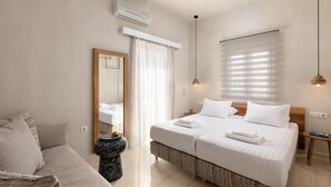 Una camera d'albergo moderna con un letto grande, una zona salotto, uno specchio e una finestra con persiane.
