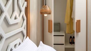 A bedroom with a bed, a wooden wall panel, a hanging light fixture, a wardrobe, and a pair of shoes.