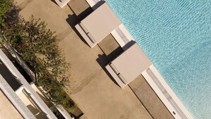 Vista aerea di un hotel con area piscina, inclusi lettini e un percorso pedonale in cemento.