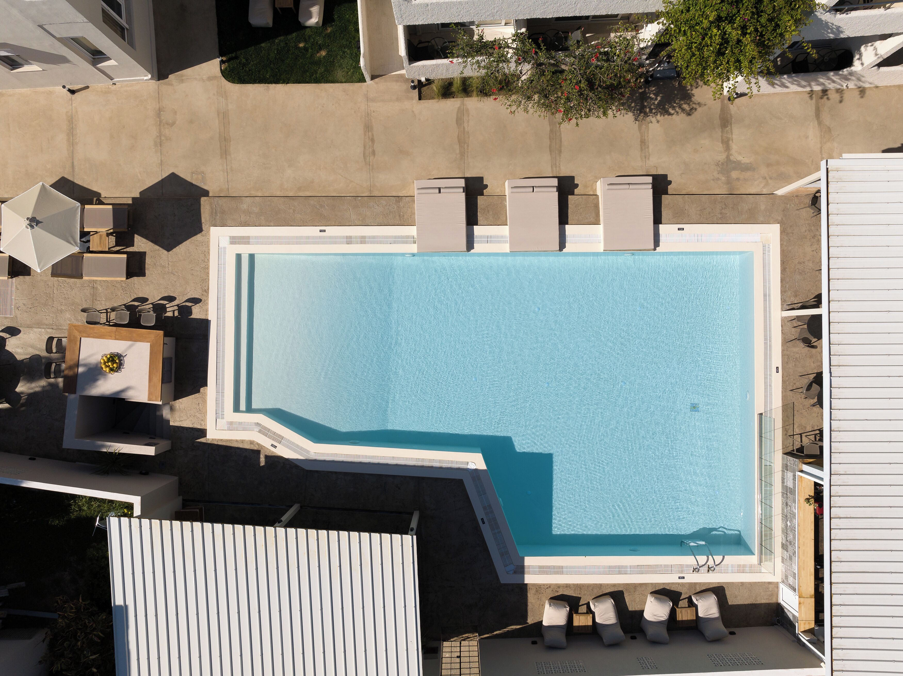 An aerial view of a rectangular swimming pool with a clear blue water surface, surrounded by a concrete deck.
