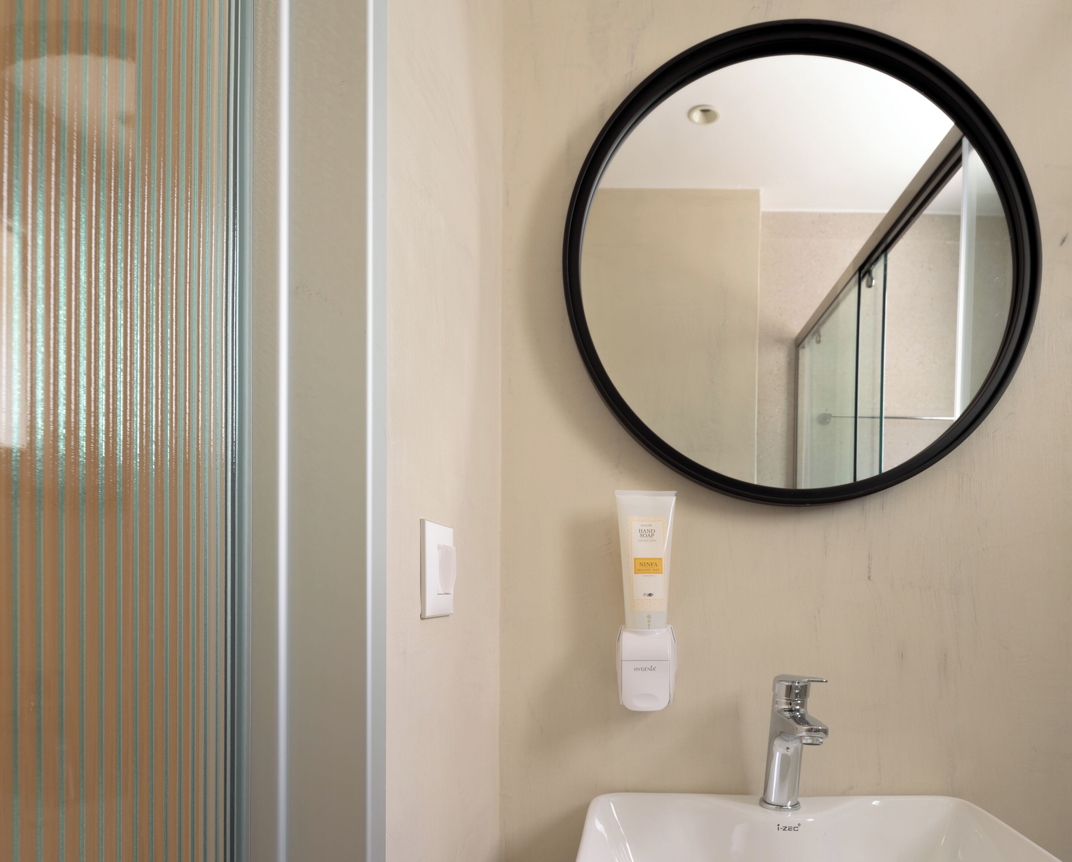 Un bagno con uno specchio rotondo, un lavandino bianco e un erogatore di sapone.