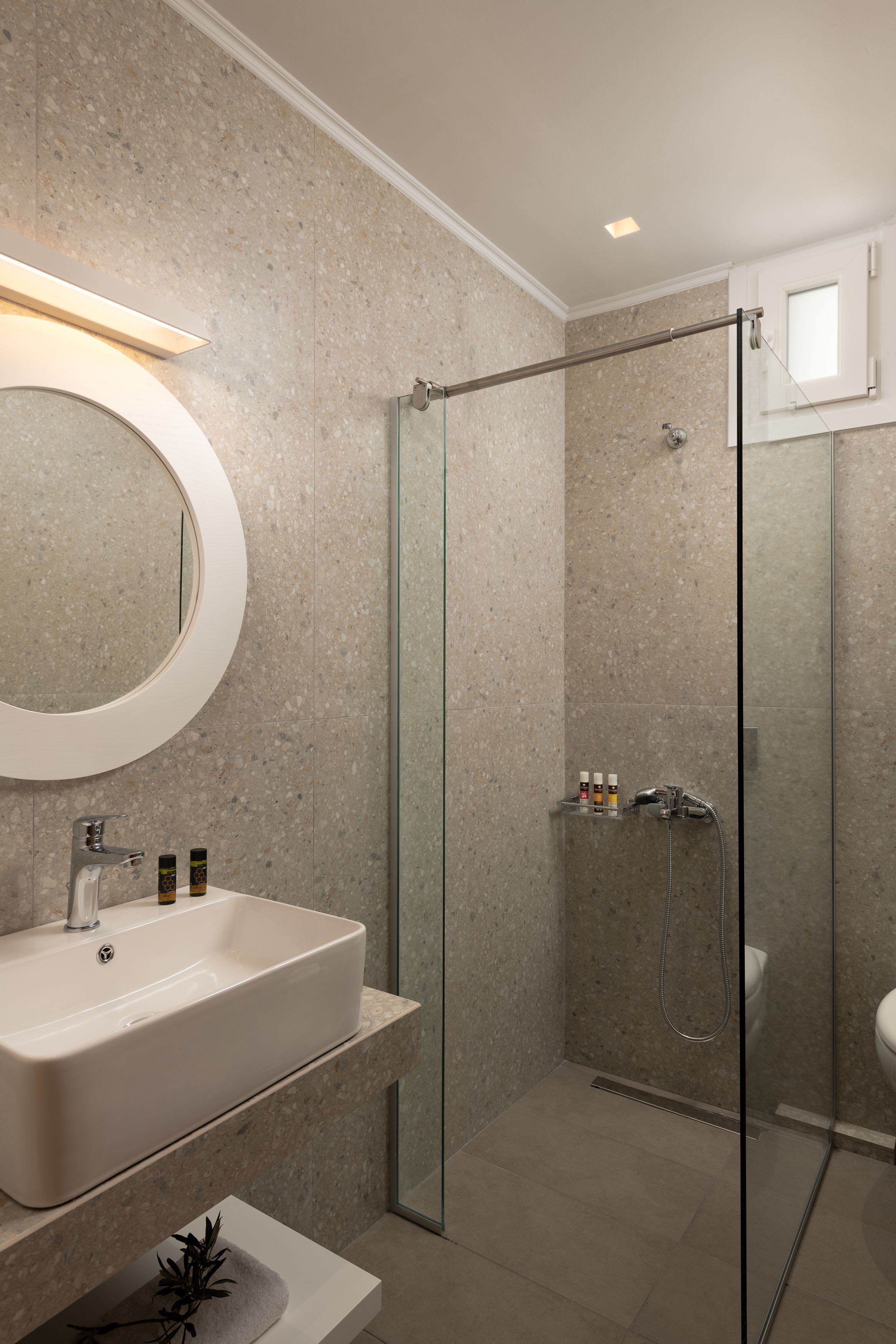 Une salle de bain moderne avec une douche à parois de verre, un miroir rond et un lavabo blanc.