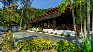 A traditional wooden building with a covered patio area, surrounded by lush greenery and a hilly landscape. - Perhentian Island Resort (Pulau Perhentian Besar)