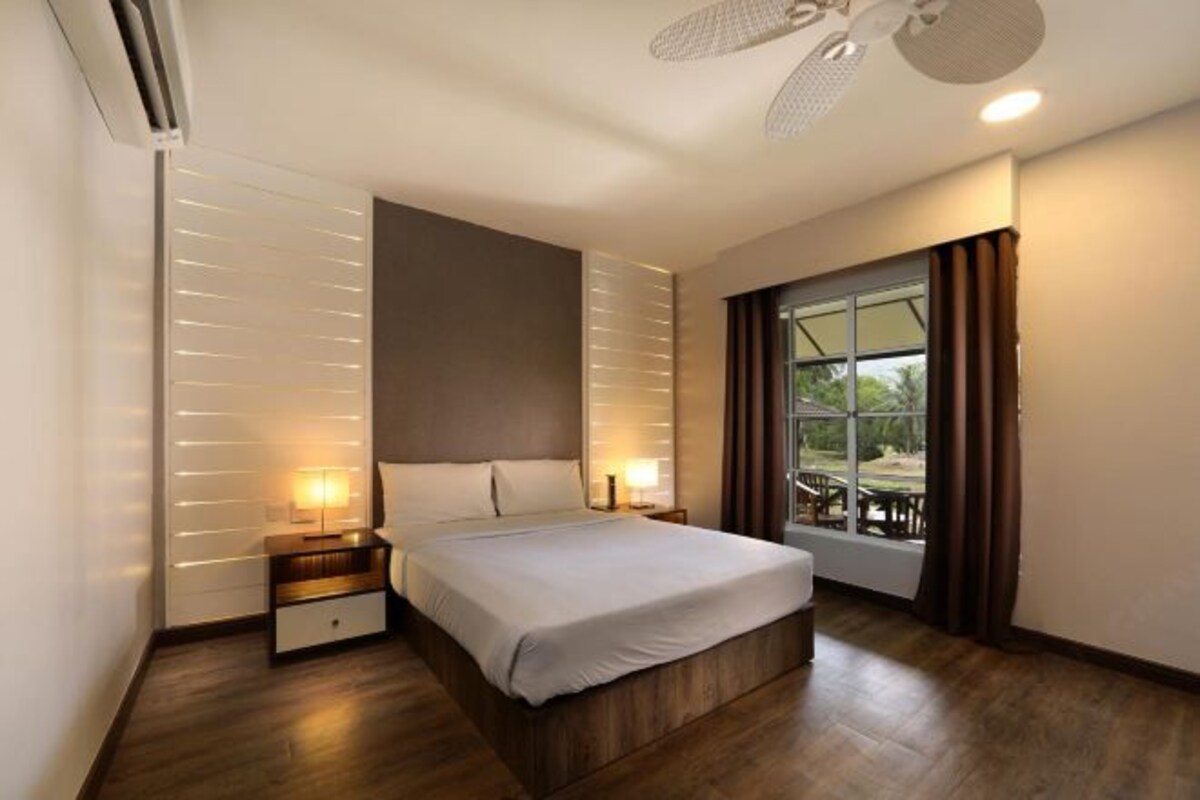 Habitación de hotel moderna con una cama grande, lámparas de noche, ventilador de techo y vistas al exterior a través de un amplio ventanal.