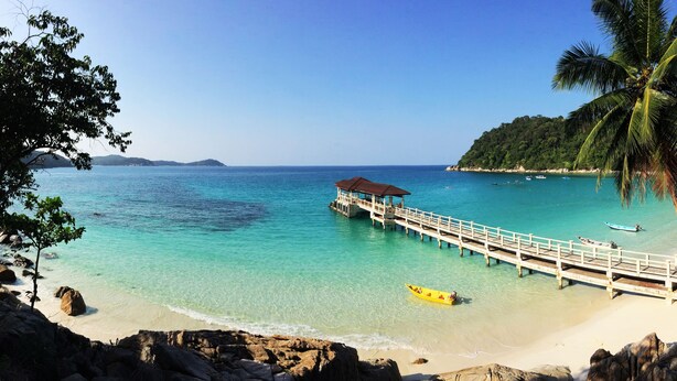 A beach with clear turquoise water, a wooden pier, and a yellow boat. - Perhentian Island Resort (Pulau Perhentian Besar)