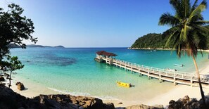 A beach with clear turquoise water, a wooden pier, and a yellow boat. - Perhentian Island Resort (Pulau Perhentian Besar)
