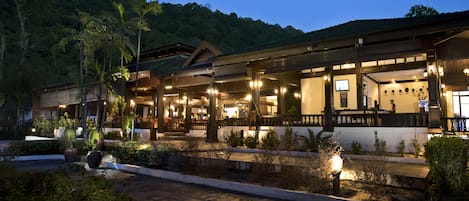 A hotel with a covered outdoor area, multiple rooms, and a view of a forested hill.