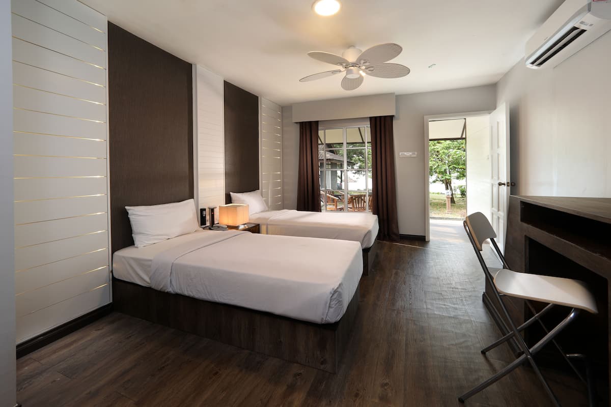 A hotel room with two beds, a ceiling fan, an air conditioning unit, and a view of the outdoors through a large window.