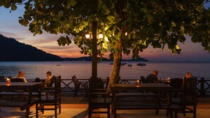 An outdoor dining area with tables and chairs, overlooking a body of water with boats and a distant island. - Perhentian Island Resort (Pulau Perhentian Besar)