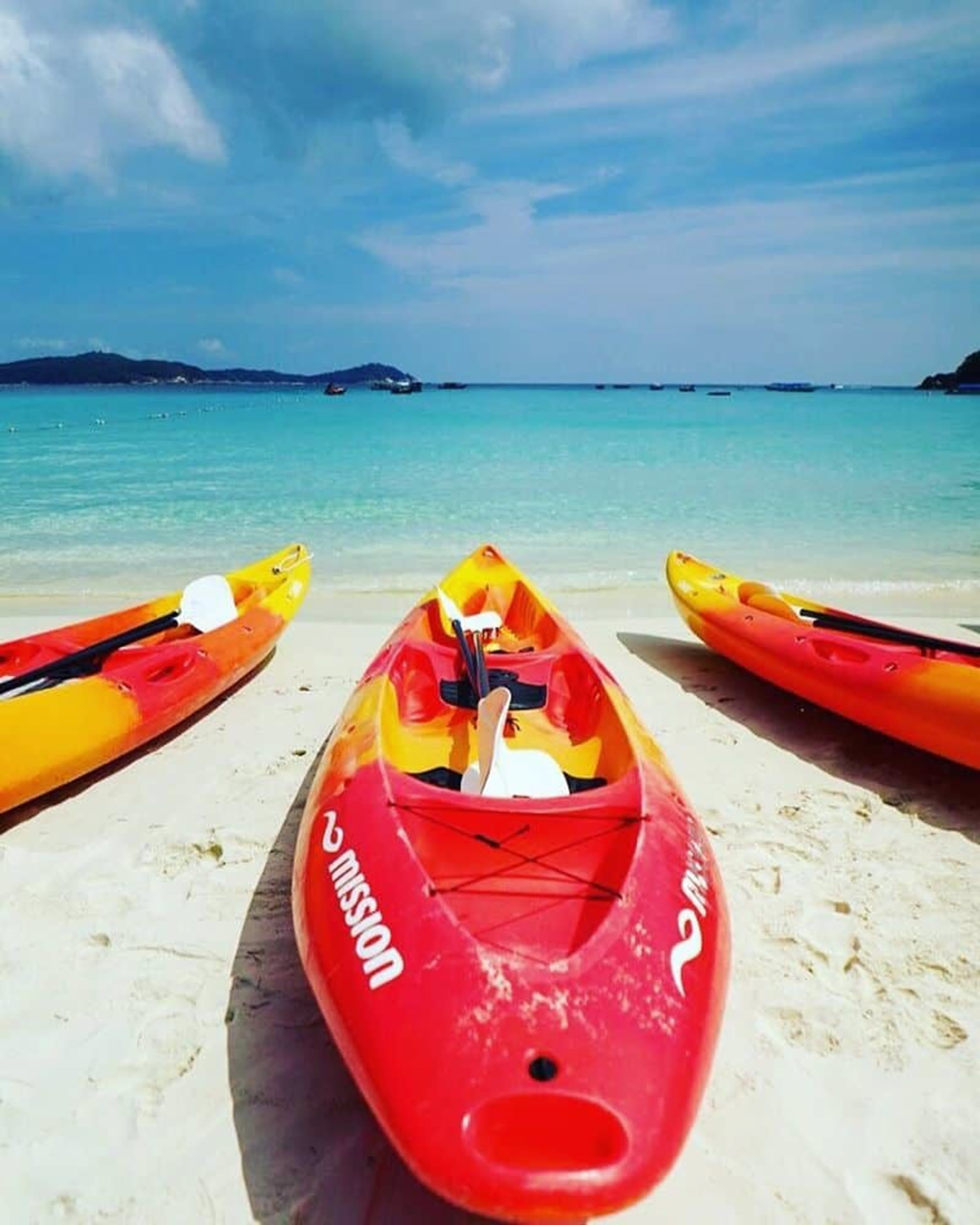 A beach with three kayaks lined up on the sand, facing the ocean.