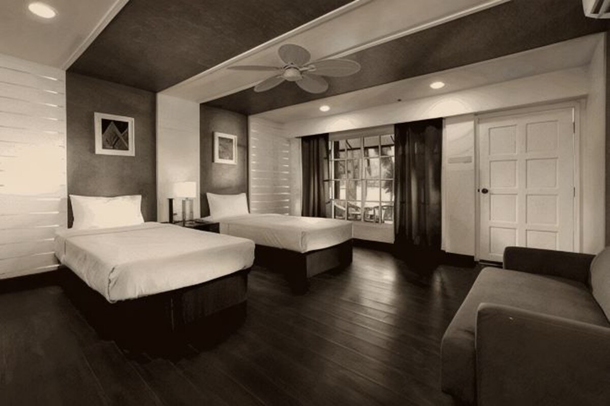 A hotel room with two beds, a ceiling fan, a large window with curtains, and a door.