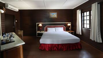 Una habitación de hotel con una cama grande, un escritorio con hervidor de agua, una mesita de noche con lámpara, una ventana con cortinas y un cuadro en la pared.