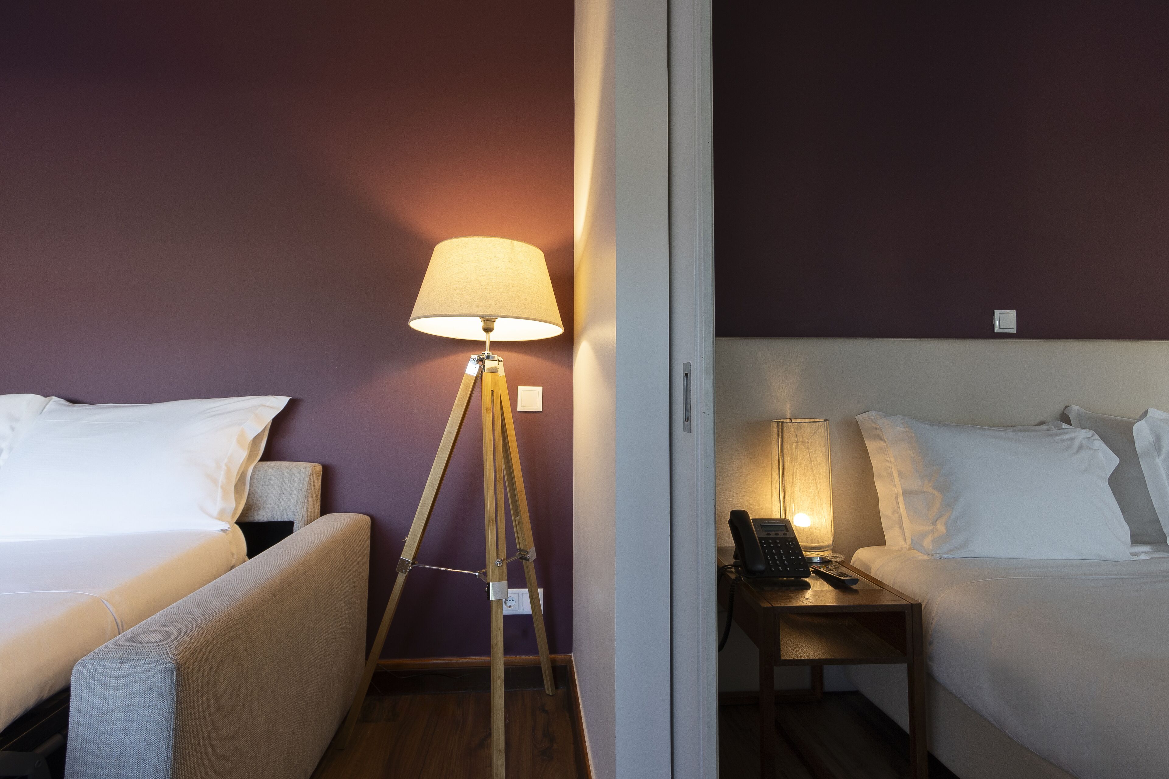 A hotel room with two beds, a bedside table with a lamp, and a floor lamp.