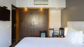 Una habitación de hotel con una cama grande, un armario de madera, un escritorio con lámpara y un refrigerador pequeño.