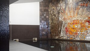 A modern interior with a reflective floor, a mosaic wall, and a geometric ceiling design.