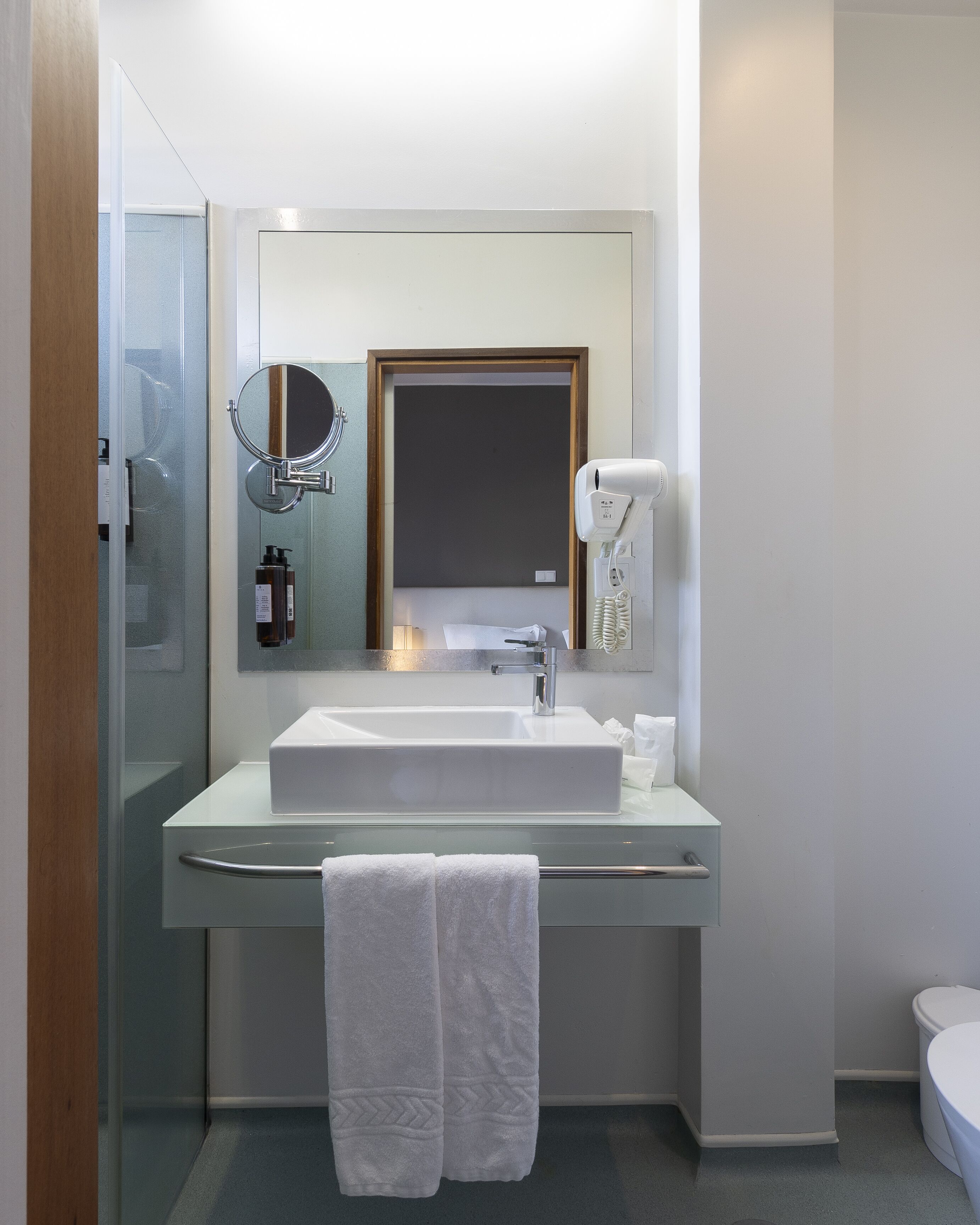 Un bagno moderno con doccia vetrata, un lavandino bianco con specchio sopra e un asciugacapelli a parete.