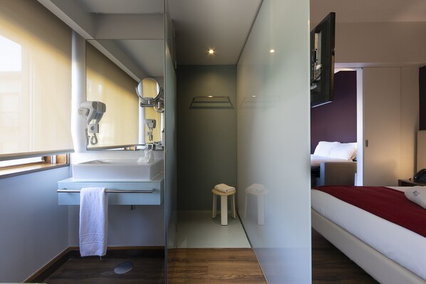 Ein modernes Hotelzimmer mit Bad, einem Bett und einem kleinen Hocker.