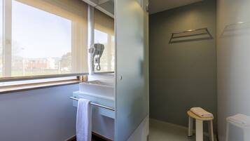 A modern bathroom with a window, a hairdryer, a towel rack, and a small stool.