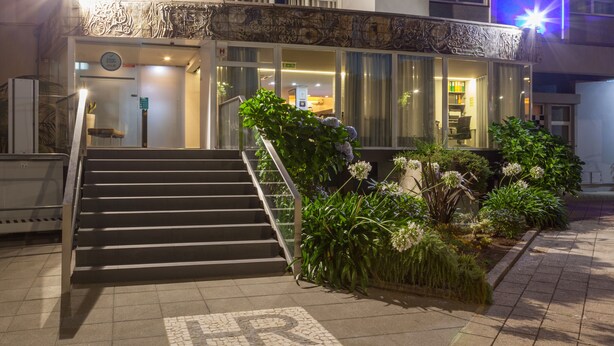 A hotel entrance with a staircase leading to the lobby, surrounded by greenery and a parking sign.